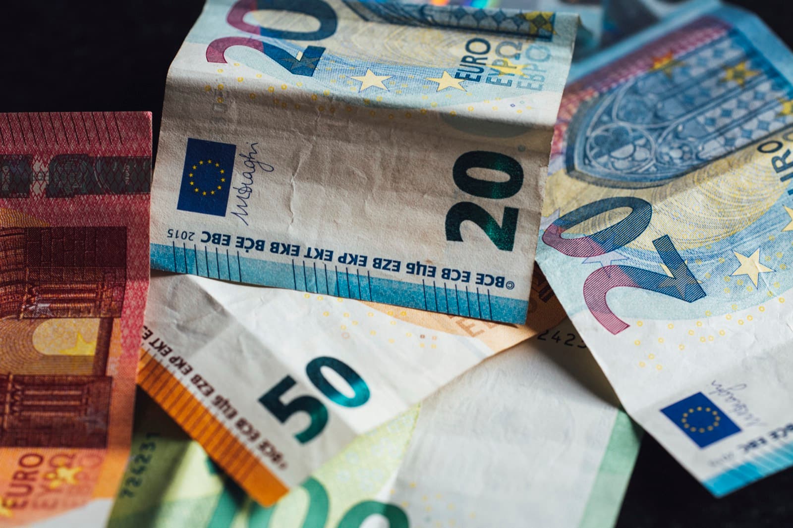 Euro banknotes of several denominations on a dark surface