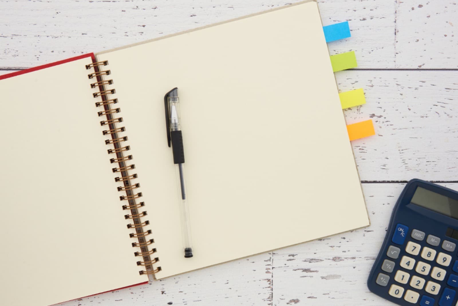 An open notebook, pen and calculator on a white desk